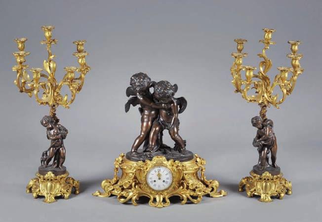 617 Garniture de cheminée en bronze ciselé, patiné et doré représentant «Les Jeux d Amour», ainsi composée : Une pendule à deux amours ailés en bronze ciselé, patiné, jouant à éteindre le feu de l