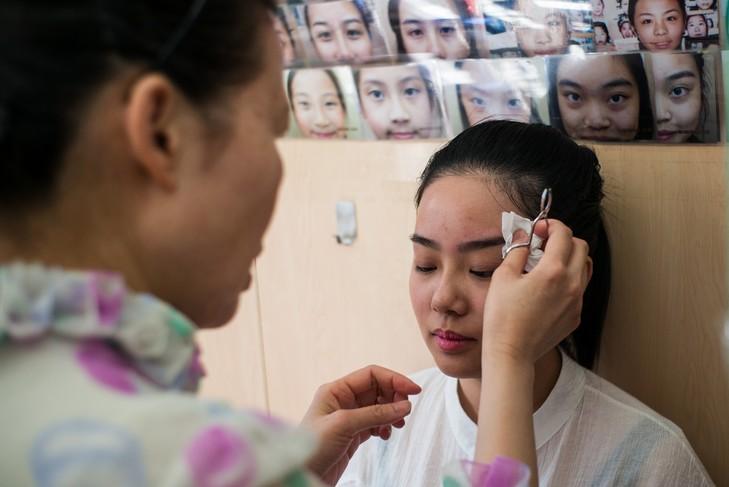 Li Chau-jing, spécialiste de l'art chinois de lire sur les visages, épile les sourcils d'une de ses patientes, le 22 juillet 2016 à Hong Kong / AFP Dans sa longue robe blanche à pois violets, elle